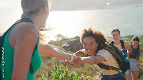 Group Of Female Friends With Backpacks Helping Each Other On Hike In Countryside On Coastal Path