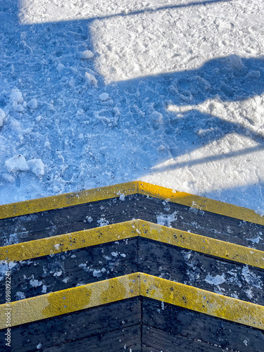 Close-up view of icy wooden steps with yellow safety strips leading into a snowy path