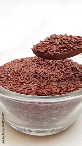 Taking out a spoonful of organic Flaxseeds with a wooden spoon from a glass bowl on a white background, Dry Linum usitatissimum, vertical clip