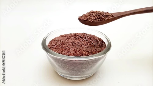 Taking out a spoonful of organic Flaxseeds with a wooden spoon from a glass bowl on a white background, Dry Linum usitatissimum