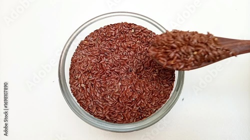 Taking out a spoonful of organic Flaxseeds with a wooden spoon from a glass bowl on a white background, top view, Dry Linum usitatissimum