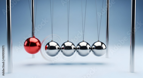 Newton's cradle momentum concept: reflective metal spheres in motion with one red ball initiating swing — physics, momentum transfer and teamwork metaphor