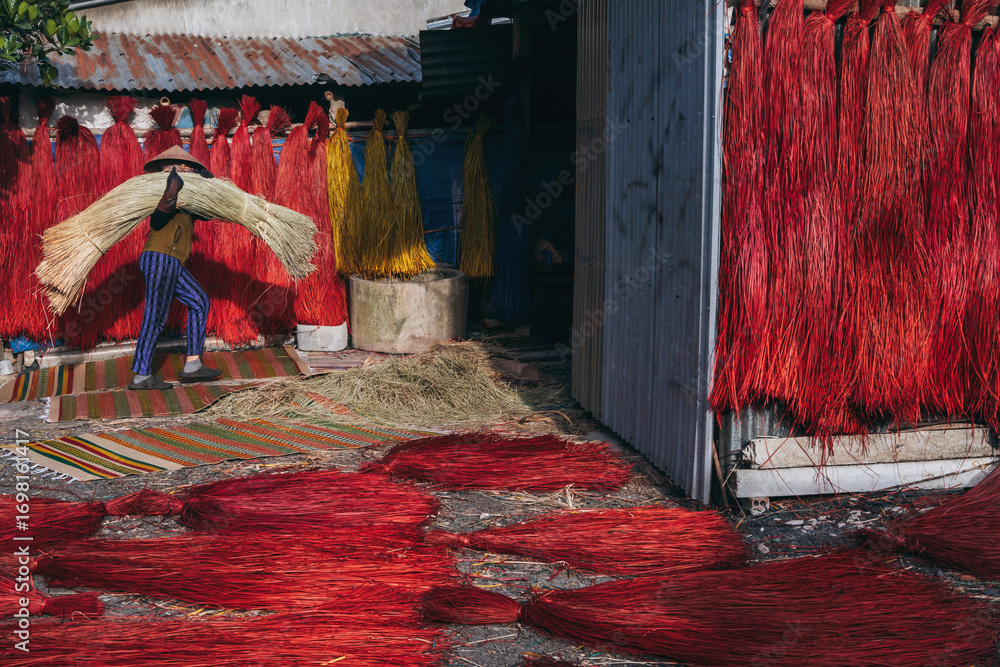 Φωτογραφία Vietnamese woman in a traditional straw hat dries dyed reeds for production of w