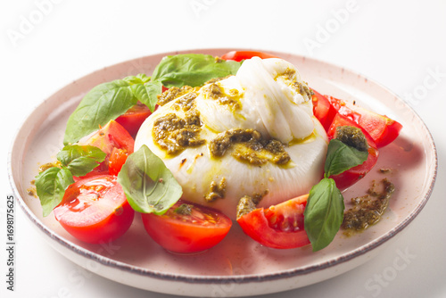 Burrata cheese caprese salad with cherry tomatoes, olive oil, pesto and seasoning. Fresh food concept. 