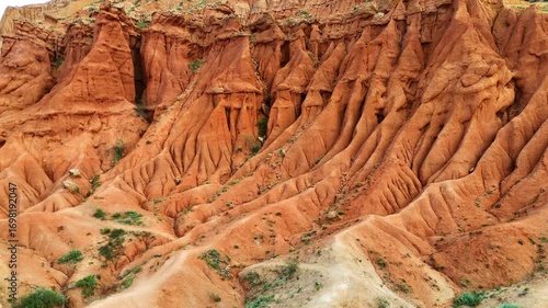 A stunning drone approach toward a massive red rock cliff in Skazka Canyon, Kyrgyzstan, highlights the unique textures, colors, and desert beauty of this dramatic natural landscape.