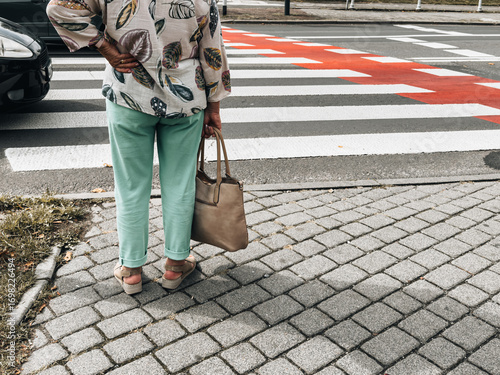 Elderly women crossing pedestrian crosswalk in city, close-up view of legs and shoes on zebra crossing symbolizing urban lifestyle, mobility and safety