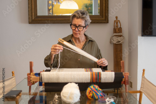 Mujer mayor sentada tejiendo en telar relajada,  medio cuerpo