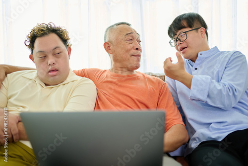 An elderly man is talking with a man with Down syndrome while holding a laptop