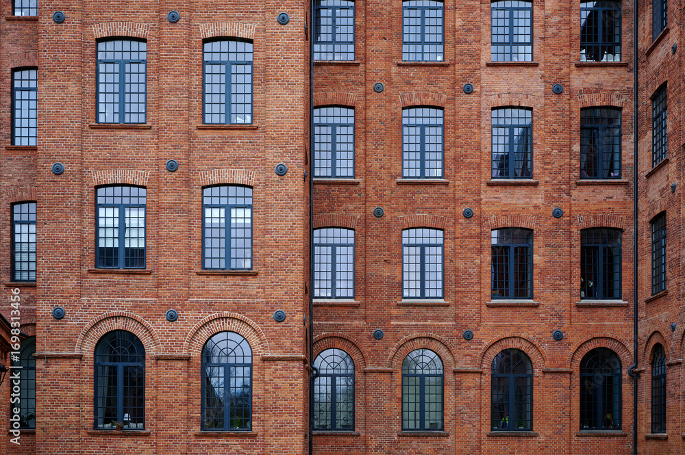 Obraz premium A facade of a restored industrial building in Łódź, Poland, characterized by rows of arched windows, black lanterns, and well-maintained brickwork, reflecting the city's industrial heritage.