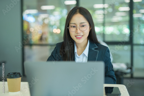 Asian businesswoman doing financial market research using laptop and digital tablet on digital investment in front of modern office.