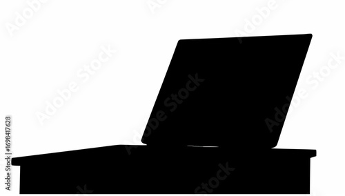 Silhouette of a laptop computer sitting on a desk with the screen slightly tilted back in a dark room