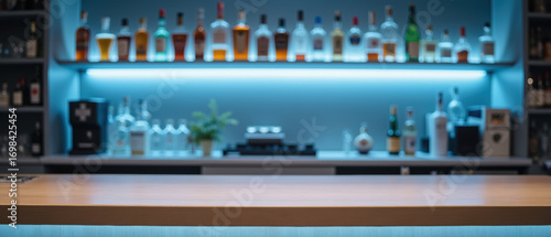Modern bar setup featuring wooden countertop, illuminated by blue lighting, with variety of liquor bottles displayed shelves. ambiance is inviting