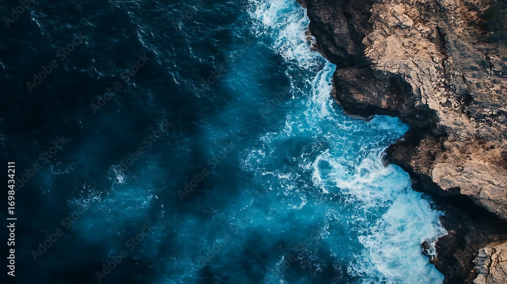 Fototapeta premium Dramatic aerial view of ocean waves crashing against rocky cliffs, creating a mesmerizing display of power and beauty from above