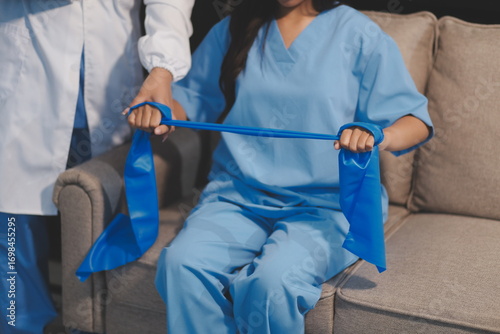 Doctor physiotherapist assisting a male patient while giving exercising treatment on stretching his arm with exercise band in the clinic, Rehabilitation physiotherapy concept