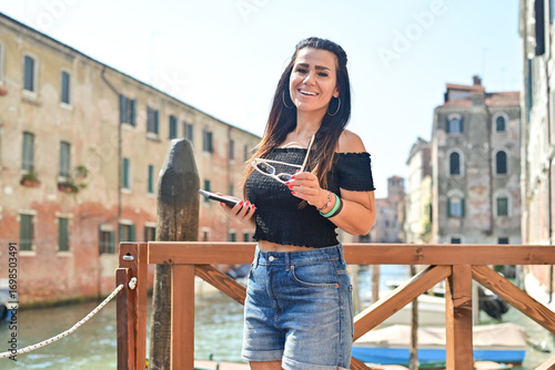 Happy smiling beautiful  Tourist  woman traveling at   Venice Italy, poses and making photos   against colorful houses. Concept of Italian gastronomy and travel. 
