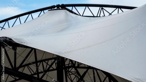 Closeup details of the fabric membrane stretching across steel framework during concert roof deployment highlighting texture and tensile architecture.