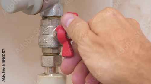 Red valve on cold water pipe to boiler for heating. Boiler heats water from cold water supply system. Man turns red valve and cut off the cold water supply to boiler