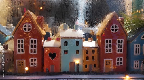 Garland and colorful ceramic houses in window of Christmas toy store. People inside toy shop chooses Christmas gifts