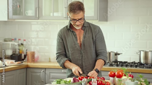 Mid adult man preparing for cooking in modern kitchen at home, wearing casual cloth. Male chef following food recipe, cleaning and slicing vegetables.