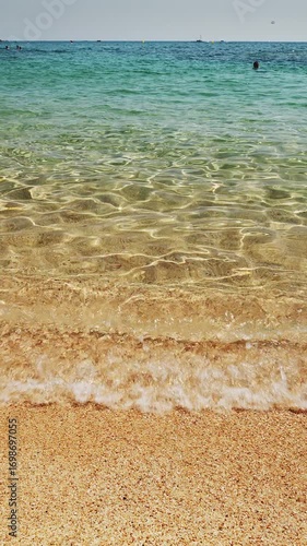 View from beach level on calm azul sea water and light waves approaching coastline.