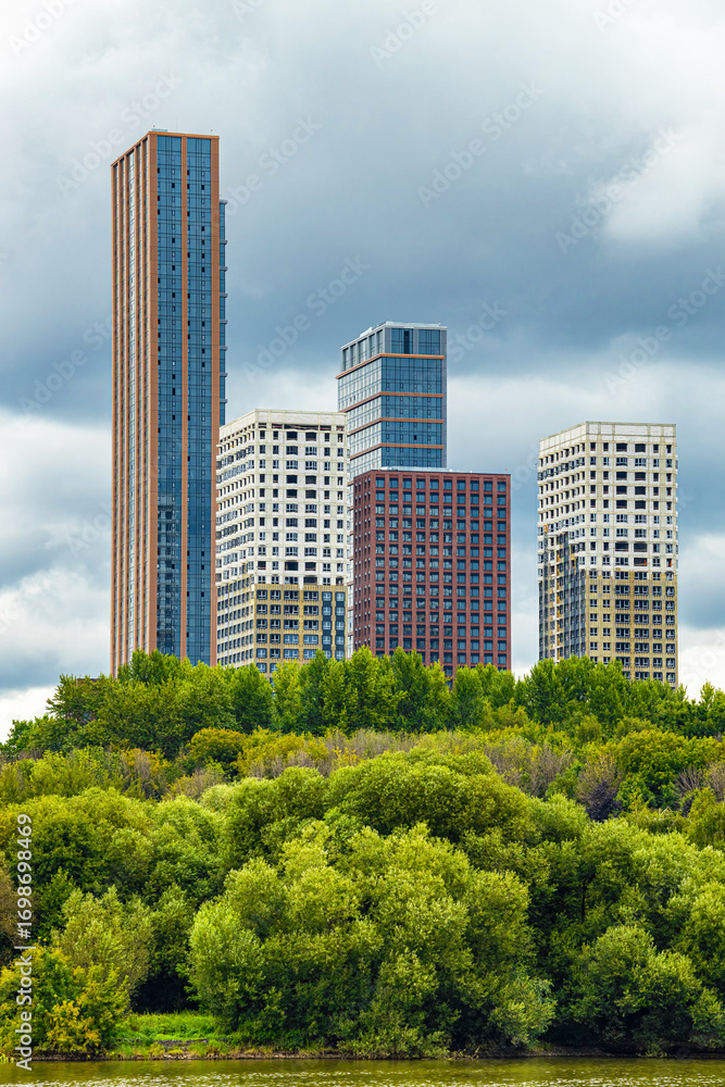 Fototapeta premium Moscow, Russia - August 18, 2025: multi-apartment residential complex near the park, vertical photo. modern residential complex against the backdrop of a gray sky. modern urban architecture. finishing