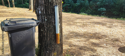 Konstfotografi Large cigarette-shaped installation on a tree beside a park trash bin