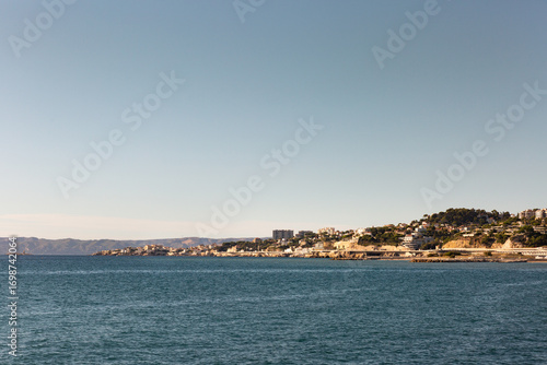 Vue sur le bord de mer de la ville de Marseille, mer au premier plan, ville ensoleillée et grand ciel bleu, rade de Marseille