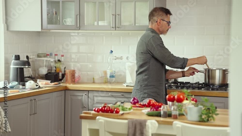 Mid adult man preparing for cooking in modern kitchen at home, wearing casual cloth. Male chef following food recipe, cleaning and slicing vegetables.