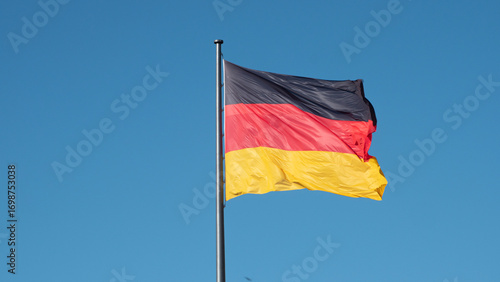 Horizontal photograph of the German flag waving in the breeze on a blue-sky day.