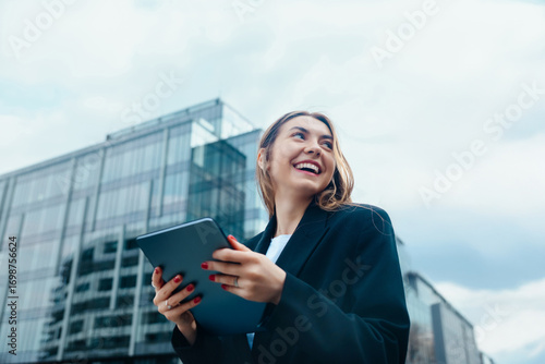 Confident young woman smiling while holding a tablet outdoors in a modern urban environment showcasing technology and communication mock up