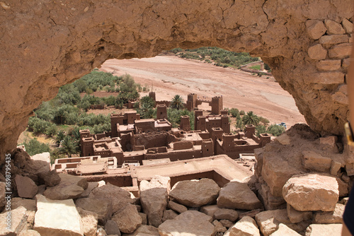 Climb to a Moroccan hilltop town - A stunning view of a traditional Moroccan fortified village and a dry riverbed from a high vantage point framed by a rocky opening.
