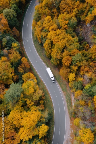 A large truck travels along a curvy road surrounded by colorful autumn trees