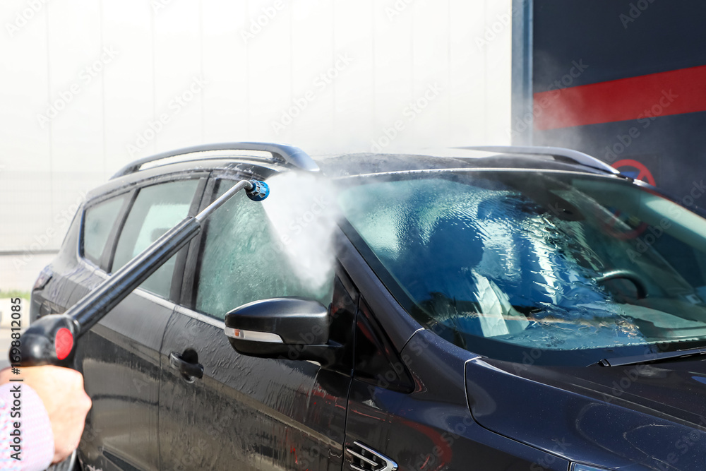 Obraz premium Car washed with a high-pressure jet under bright sunlight, emphasizing sparkling cleanliness, professional maintenance, and contemporary vehicle care (part of the “at the car wash” series).
