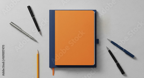Organized workspace flat lay featuring a vibrant orange and blue notebook surrounded by various writing instruments on a clean, minimalist background, perfect for creative planning and daily tasks