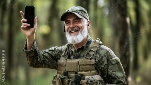 Smiling Veteran in Camouflage Holds Phone Outdoors, Positive Communication Concept