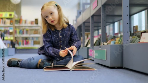 4 year old girl sitting on the floor in municipal library and reading a book