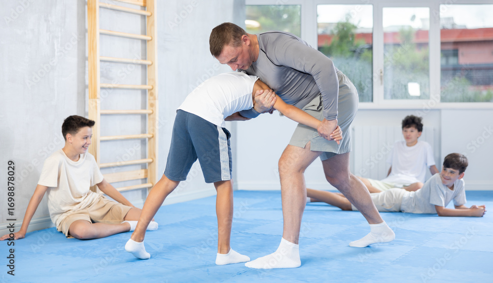Obraz premium Proficient male instructor teaching his underage students self-defense methods during workout session