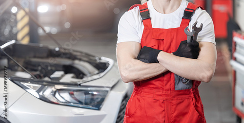 Schilderij op canvas Auto mechanic in red overalls holding wrench in service garage, banner