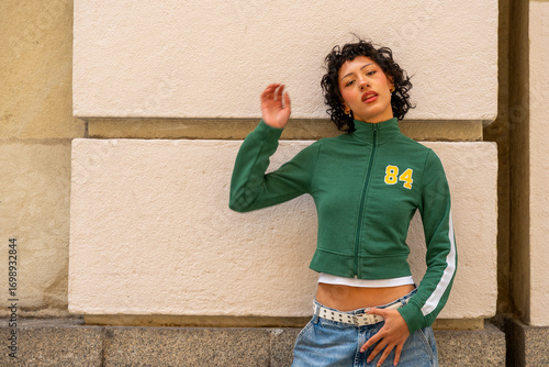 Young woman posing against a wall wearing green jacket and jeans