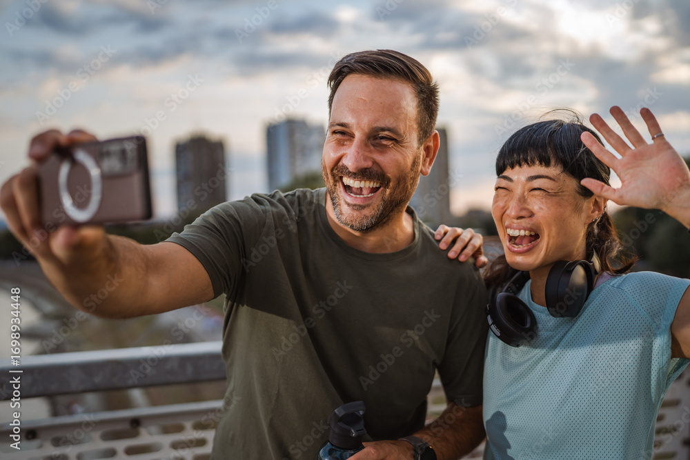 Fototapeta premium Happy couple taking a selfie after workout on city bridge