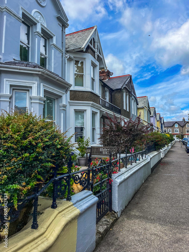 Douglas, Isle of Man 08,05,2023 Row of houses with a white fence and a bench in front of one of them. The houses are all different colors and sizes Isle of Man -