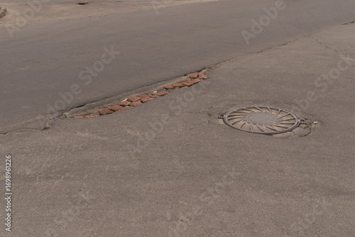 Damaged Asphalt Road showcasing Exposed Bricks in an Urban Environment Needs Repair. The image shows a damaged road section with exposed bricks, highlighting serious infrastructure issues in the area