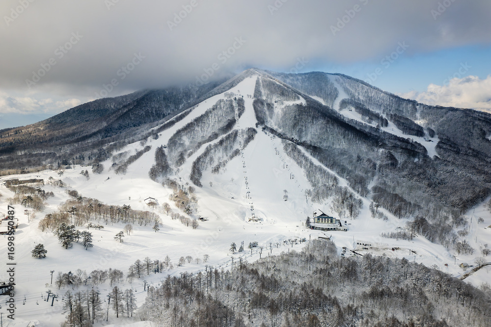 Obraz premium Wide shot of snow-covered ski slopes, chairlifts, and forests at a Japanese resort