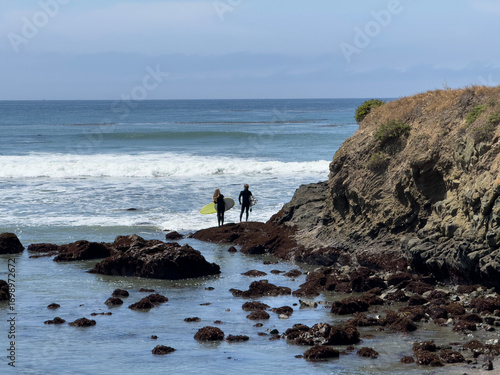 Silhouette of two surfers in wetsuits looking to jump in the water, but checking the waves first.