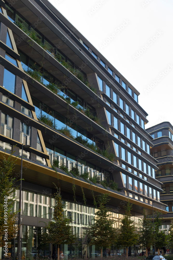 Obraz premium A large, modern building with numerous windows is beautifully surrounded by lush trees in a vibrant urban environment