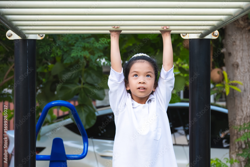 Fototapeta premium Portrait of Happy girl swinging on the monkey bars in playground. Exercise for health of 8-9 year old Asian girls.