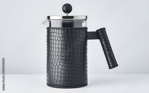 The photograph features a modern French press coffee maker with a sleek, stylish design, primarily black with a textured leather-like pattern.