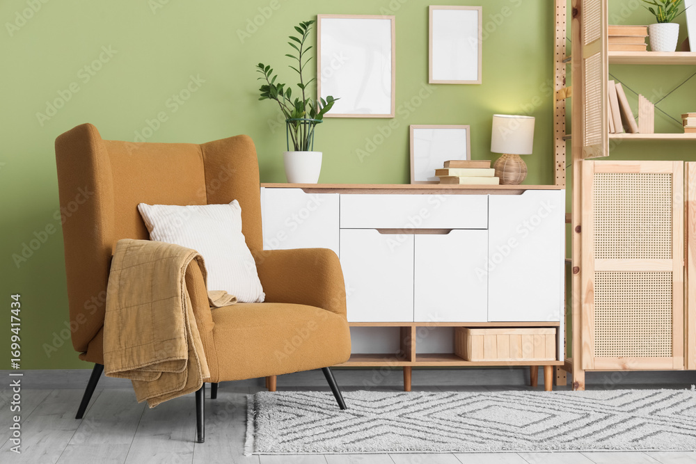 Fototapeta premium Interior of living room with comfortable armchair, chest of drawers and book shelf, closeup