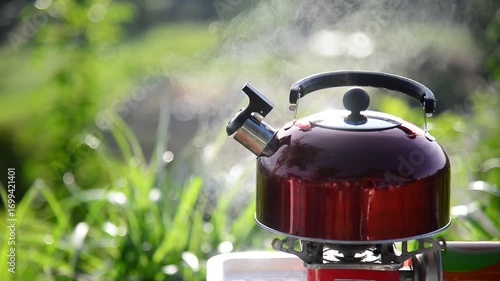 The hot water kettle has steam coming out after the kettle is placed on the gas stove to boil water for drip coffee to friends who are camping together 