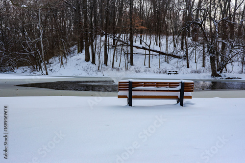 Snow covered bench overlooking partially frozen water